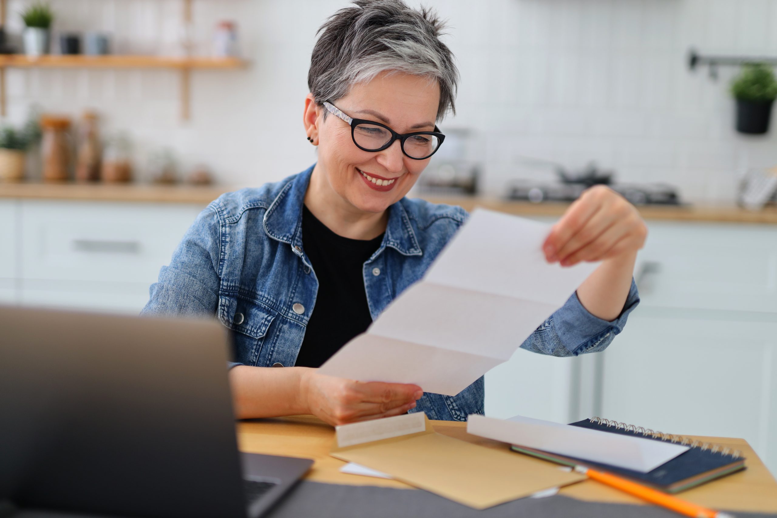 Smiling mature woman reading a letter about the coverage basics of her health insurance.