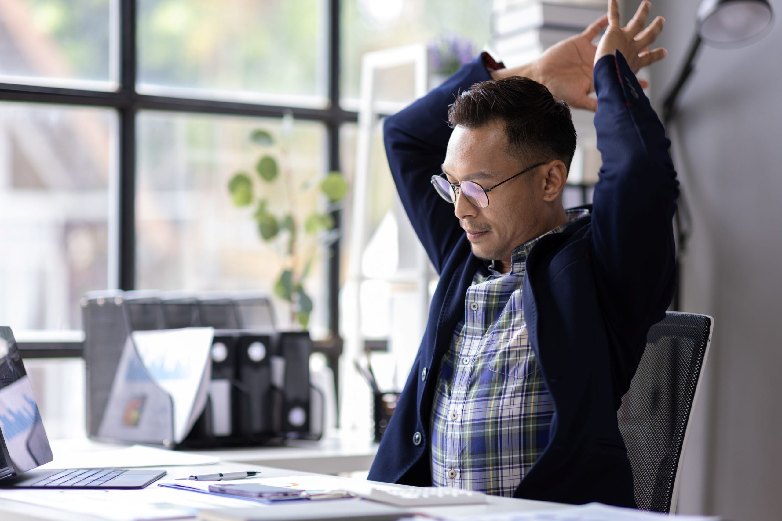 A man sitting at his work desk, stretching his arms over his head.