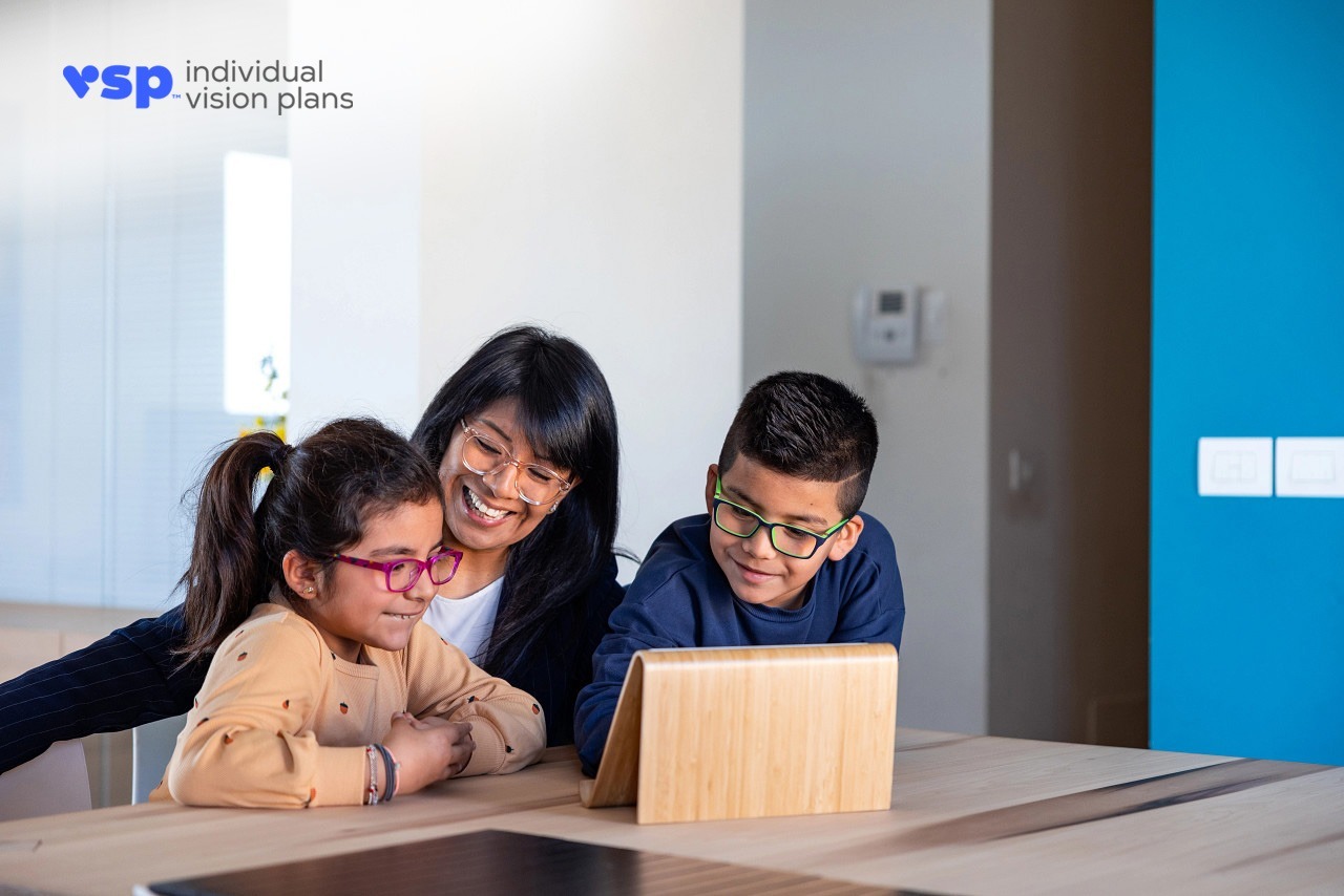 A mother, daughter and son wearing glasses, sitting at home and looking at a computer and learning about VSP® vision care.