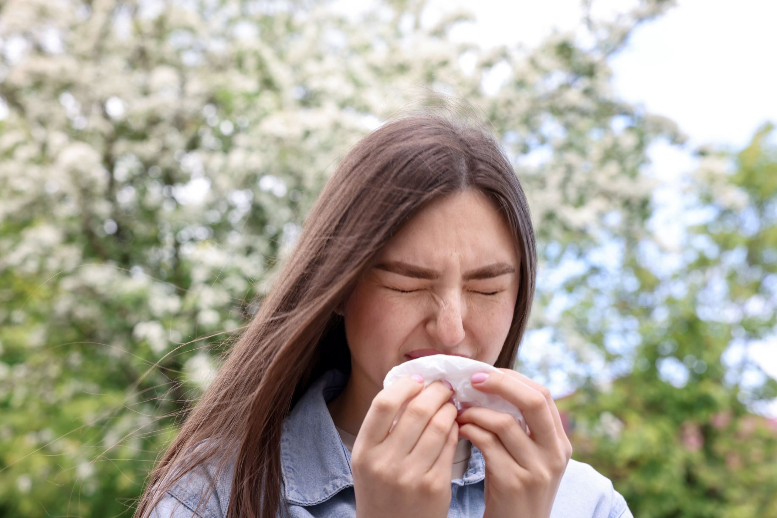 A young woman in an Idaho park sneezing from a spring allergy.